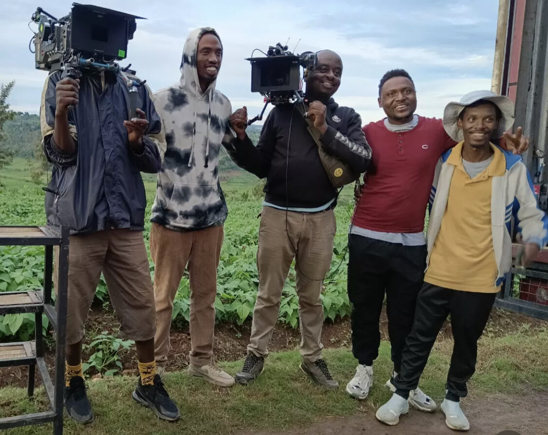 Caleb Mwenedata and a film crew of five posing outdoors with cinema cameras beside a green field