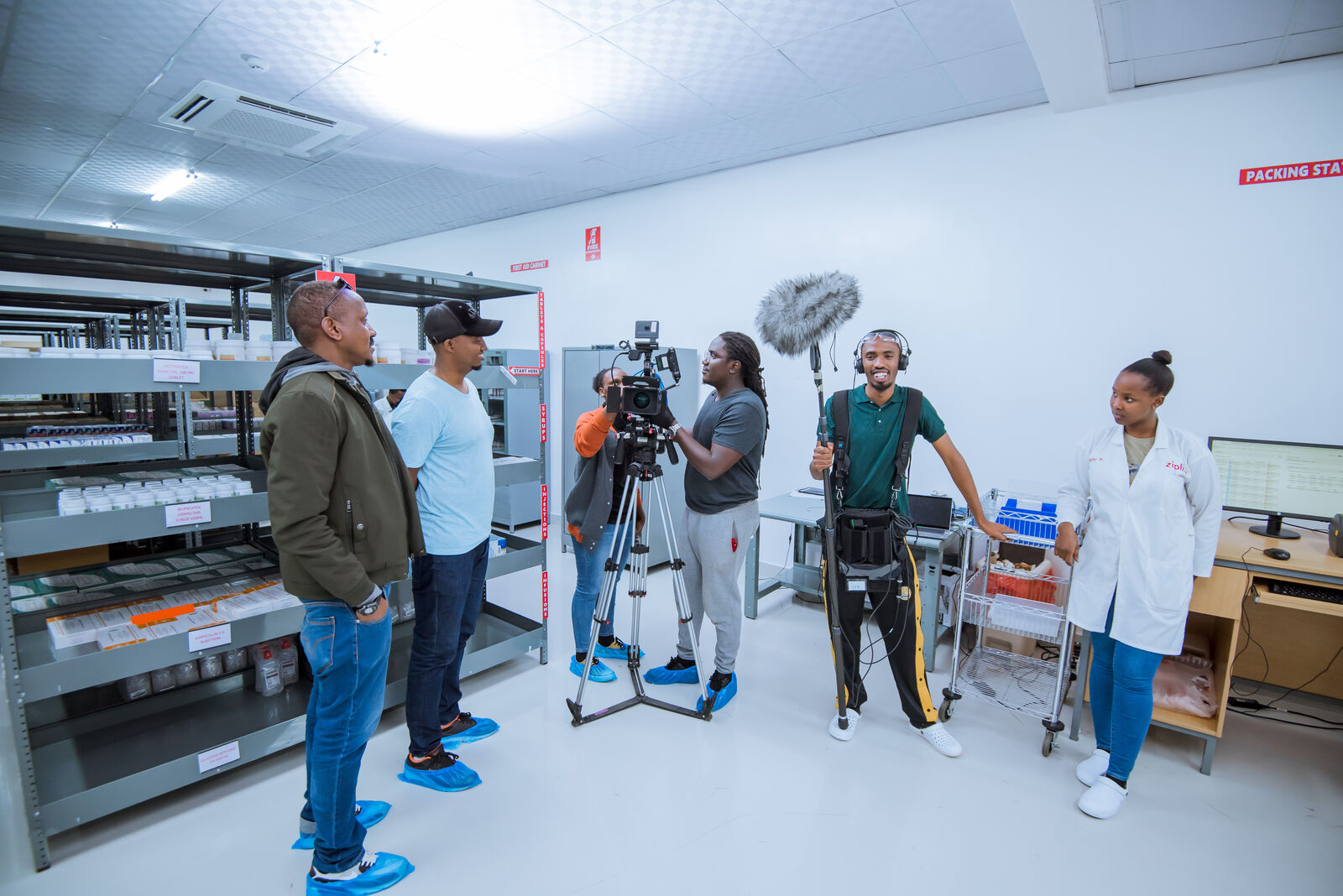 Film crew recording an interview in a laboratory, with a camera on a tripod and a boom microphone operator
