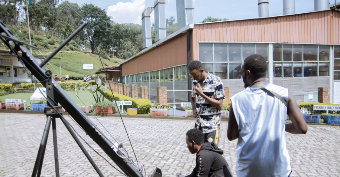Crew members setting up a camera jib crane on a paved courtyard outside a factory building
